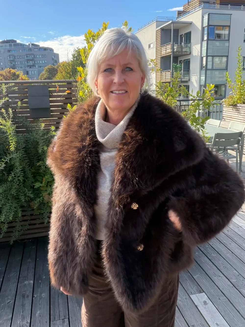 Kvinne i brun fuskepelsjakke på en solfylt takterrasse