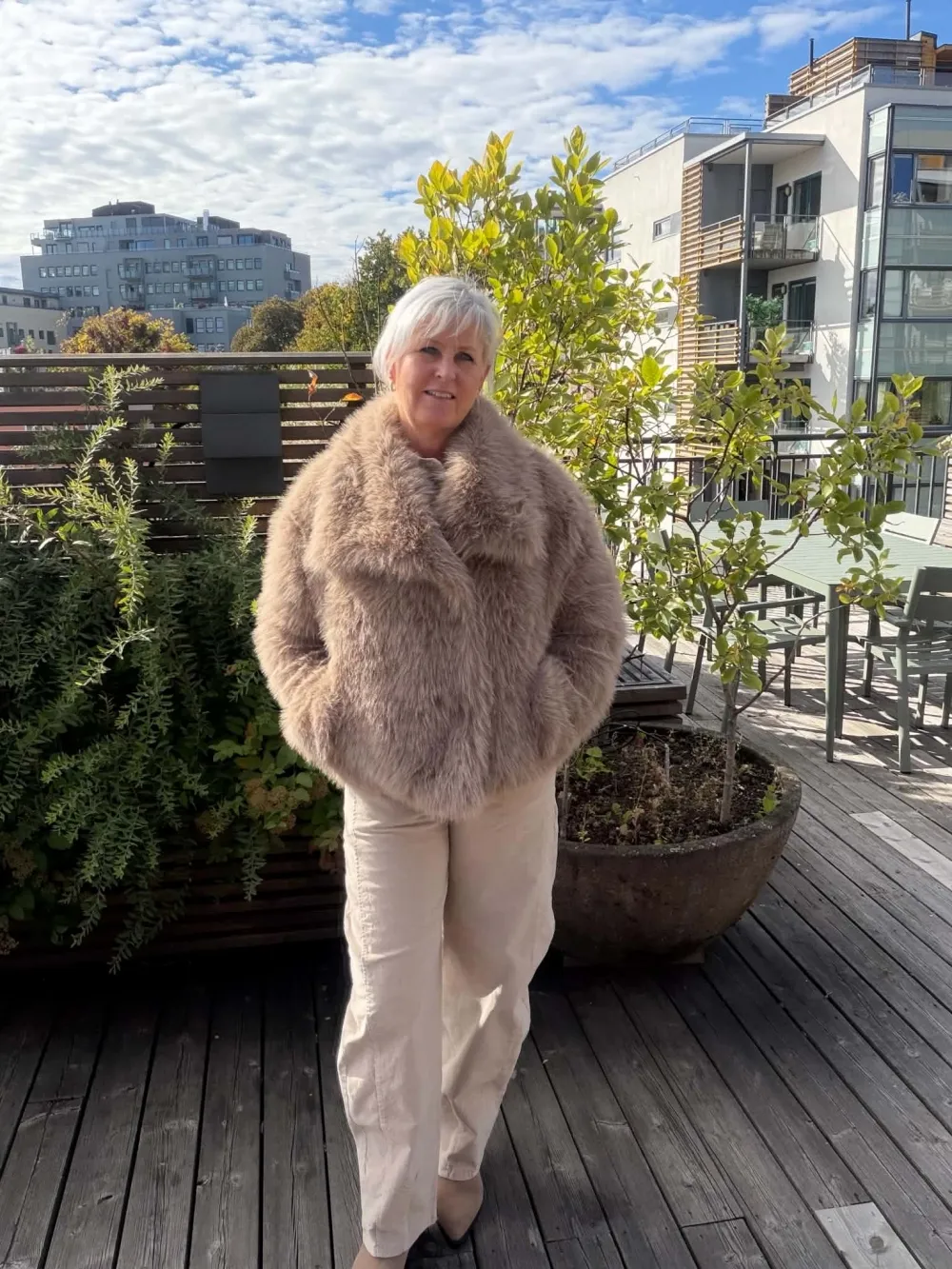 Kvinne i taupe fuskepelsjakke på en takterrasse