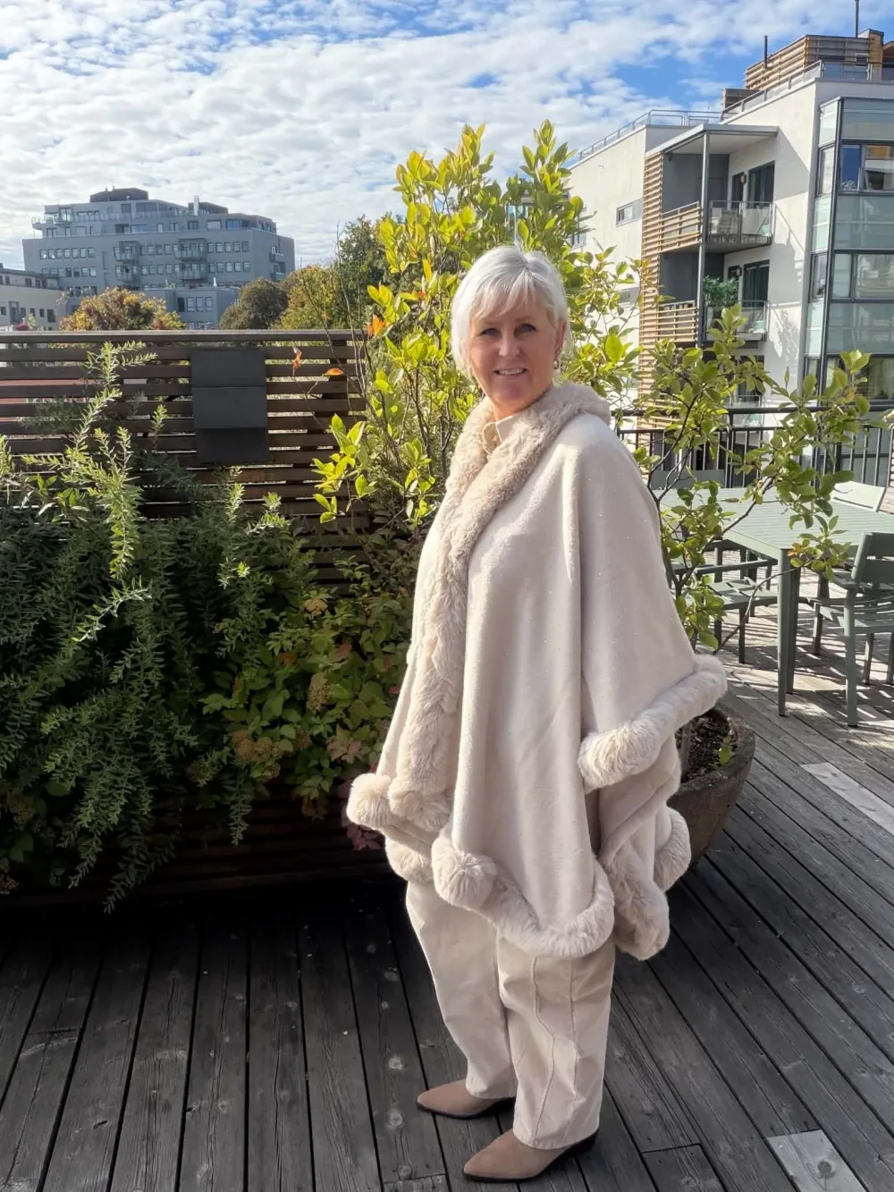Kvinne i kremfarget ponchosjal med pelskant
